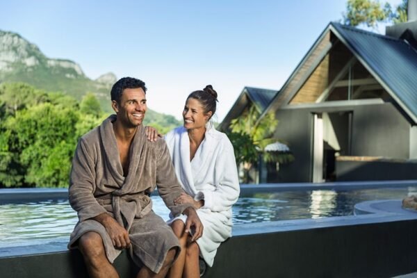Happy couple in bathrobe sitting at the edge of swimming pool